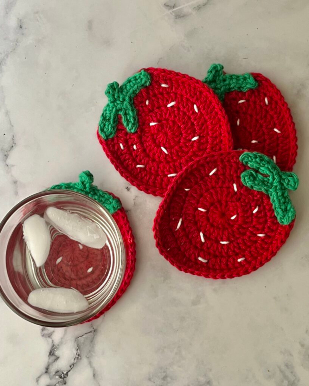 four crochet strawberry coasters with glass of water on top