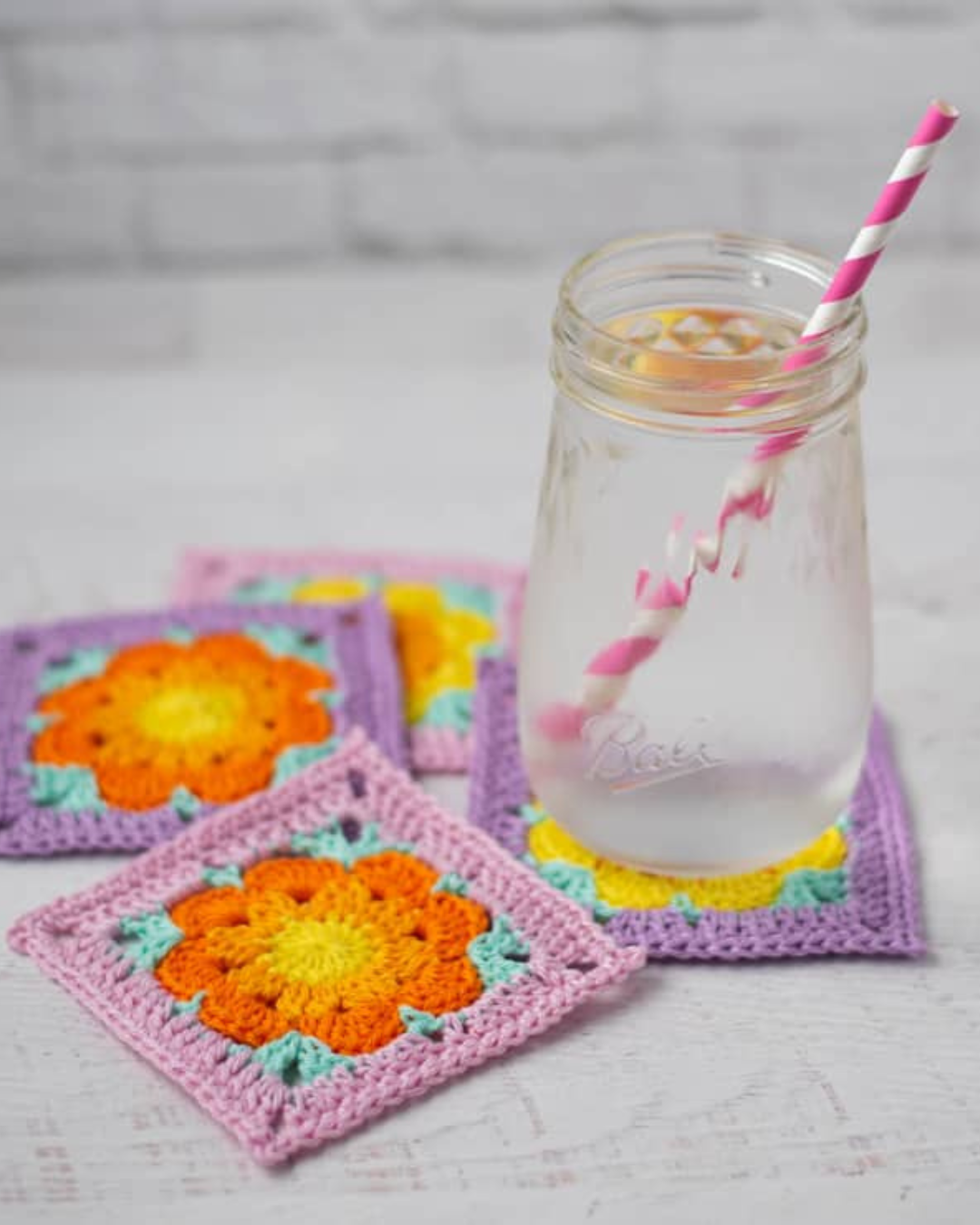 Four colorful crochet flower coasters with lemon water glass on top